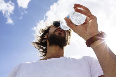 Low angle view of man wearing sunglasses and drinking water against sky