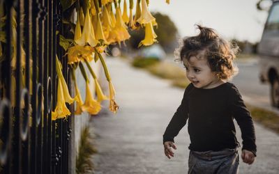 Cute smiling girl standing on footpath by yellow flowers 