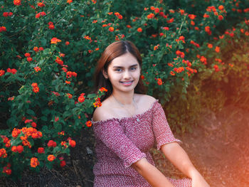 Portrait of smiling young woman standing by flowering plants