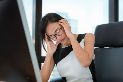 Woman with head in hand sitting on chair by window in office