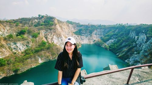 Portrait of young woman standing on railing against mountain