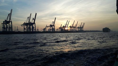 Cranes at commercial dock against sky during sunset