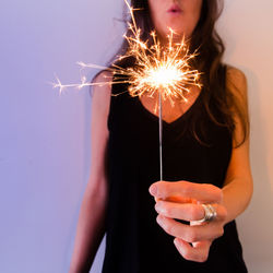 Close-up of woman holding sparkler against sky