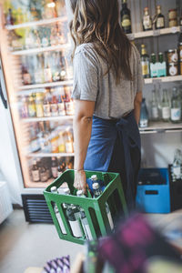 Female employee carrying bottles in crate at deli