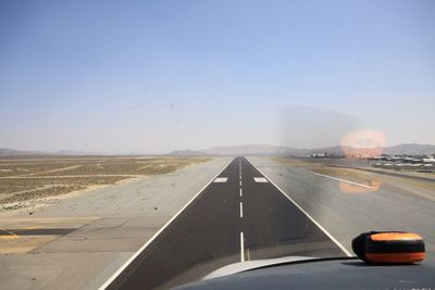 Runway seen through airplane windshield against clear blue sky