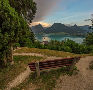 Empty bench by lake against sky
