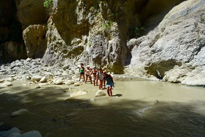 Group of people wading in river against rock formation