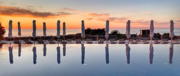 Reflection of wooden posts in swimming pool against sky during sunset