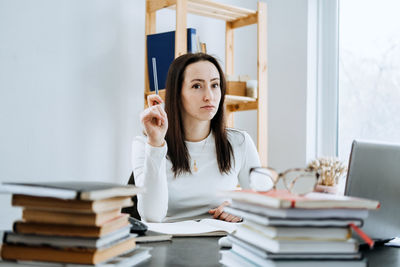 Female accountant working with many books and notepads on the background of laptop and calculator.