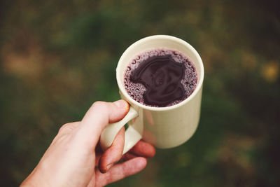 Cropped hand holding grape juice in cup