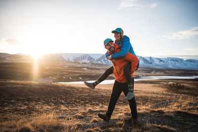 Man carrying woman on piggyback in field with mountains in background