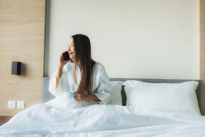 Young woman sitting on bed at home