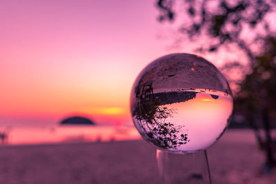 Close-up of crystal ball on glass against sky during sunset