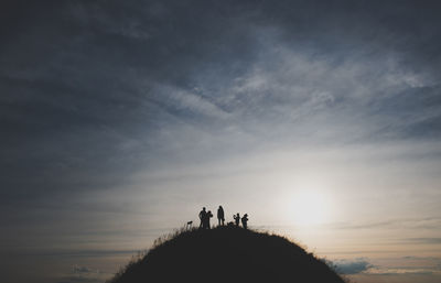 Silhouette people on land against sky during sunset