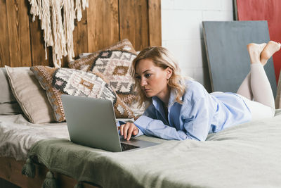 A girl with blond hair is lying on a bed in front of a computer.