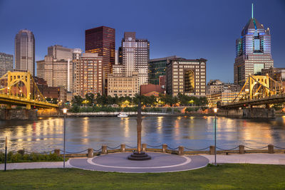 Illuminated buildings by river against sky in city