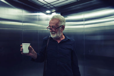 Man holding coffee cup while standing in elevator