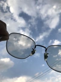 Cropped hand of person holding eyeglasses against sky