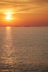 Commercial ships anchored at sea at sunset.