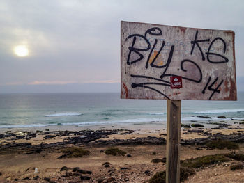 Information sign on beach against sky