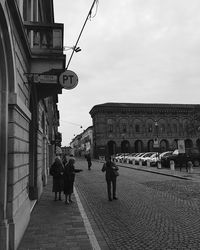 Rear view of people walking on street amidst buildings in city