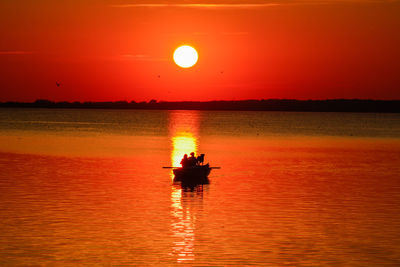 Silhouette people on boat sailing in sea against sky during sunset