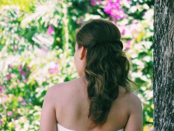 Rear view of bride standing by tree trunk