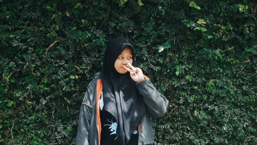 Young woman gesturing while standing by plants at park