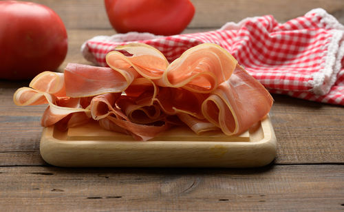 Sliced thin slices of prosciutto on wooden brown board, wooden table background