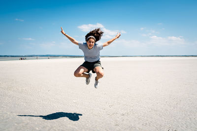 Portrait of teenage girl jumping at beach against sky