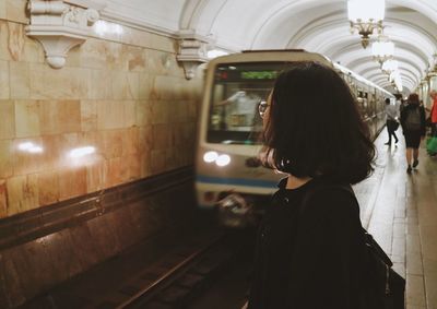 Side view of woman standing against train at subway station