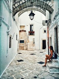 Side view of woman sitting on steps in alley