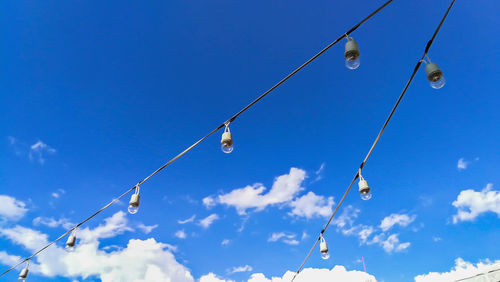 Low angle view of light bulbs hanging against blue sky