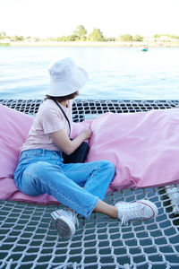 Full length of young woman sitting on bridge over water