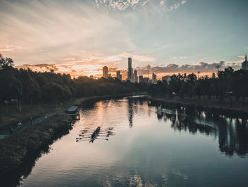 Scenic view of lake by buildings against sky during sunset