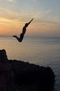 Backlit boy with sunset in the background jumping from a rock into the mediterranean sea