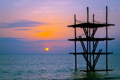 Silhouette crane by sea against sky during sunset