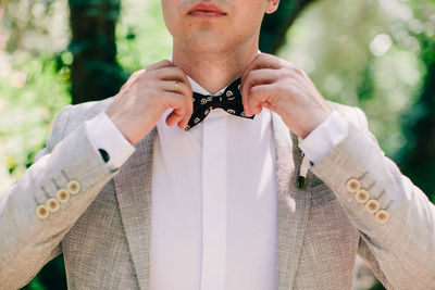 Midsection of man adjusting bowtie outdoors