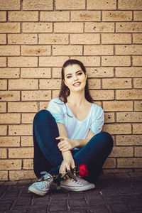 Portrait of young woman sitting against brick wall