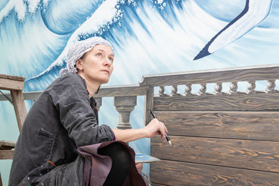 Mature woman artist draws thoughtful looking at her work - a mural on the marine theme