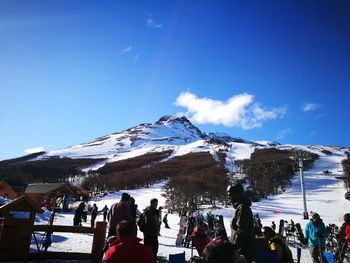 People on snowcapped mountain against blue sky