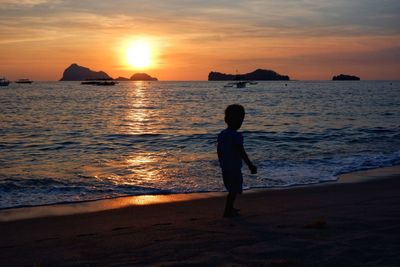 Silhouette boy on beach against sky during sunset