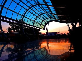 Reflection of silhouette buildings on glass against sky during sunset