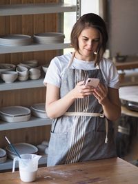 Smiling woman using mobile phone at kitchen