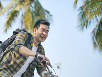 Smiling man sitting on bicycle against palm trees