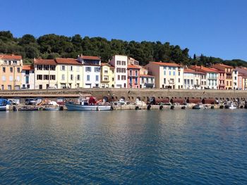 Boats in river by buildings against clear blue sky