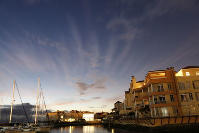 Buildings by river against sky during sunset