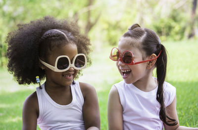 Two little girls african american and caucasian laughing with wearing funny sunglasses in park. 