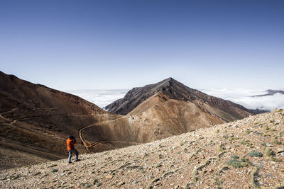 Rear view of man walking on mountain against clear sky