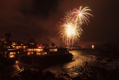 Illuminated fireworks over beach against sky in city at night